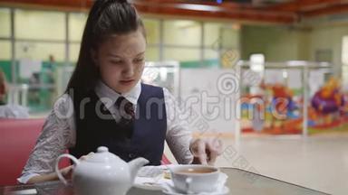 穿着校服的少女坐在<strong>学校食堂</strong>的桌子旁吃蛋糕，喝茶。